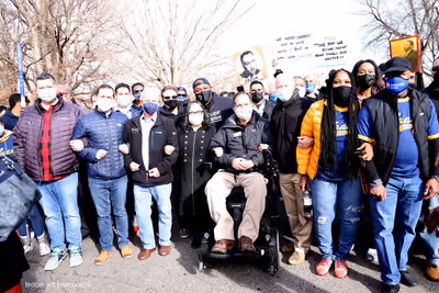 Chris interlocking arms with a large group of elected officials at a Marade with Martin Luther King signs in the background